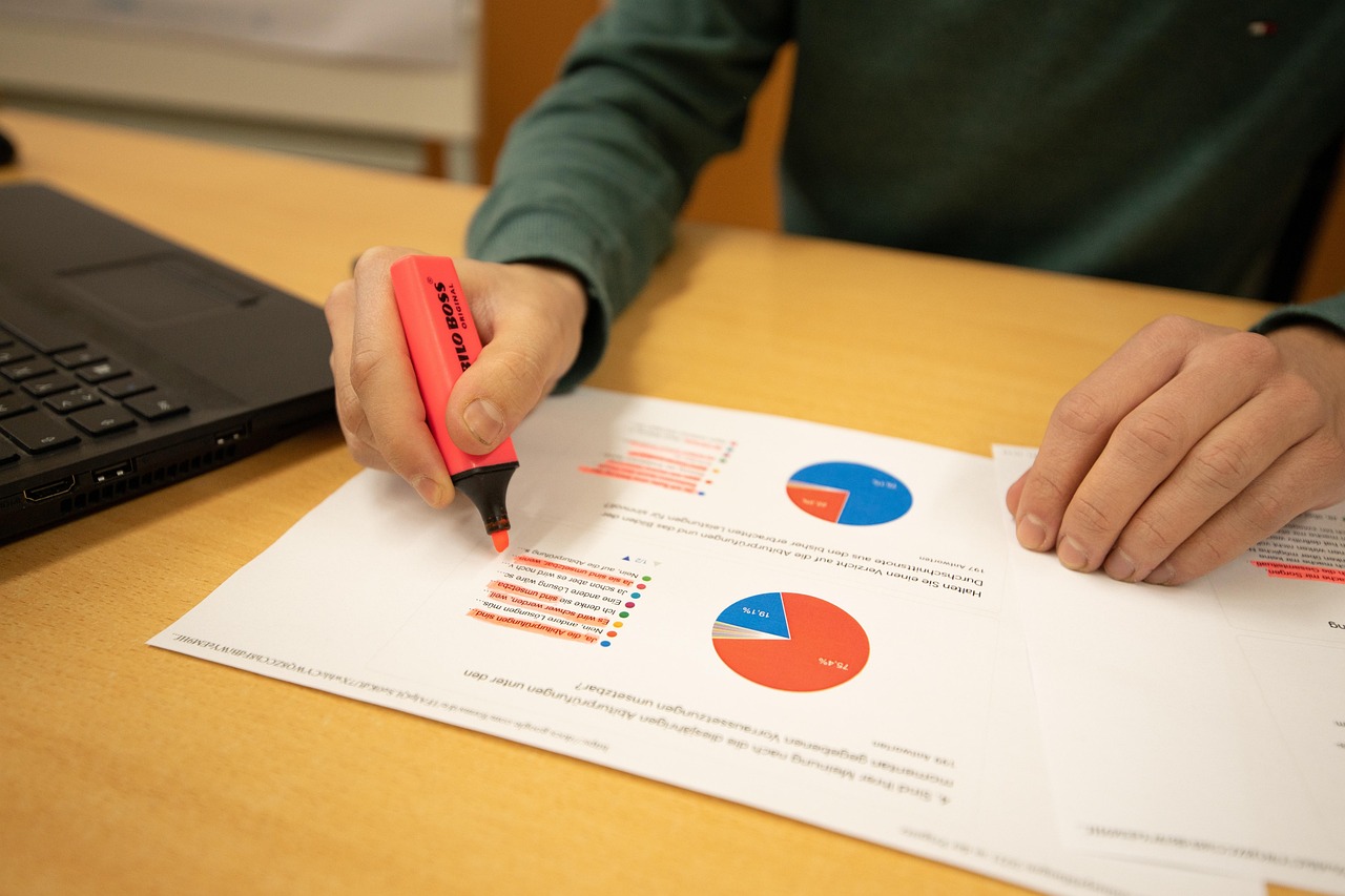 A person highlighting data and charts on a document next to a laptop