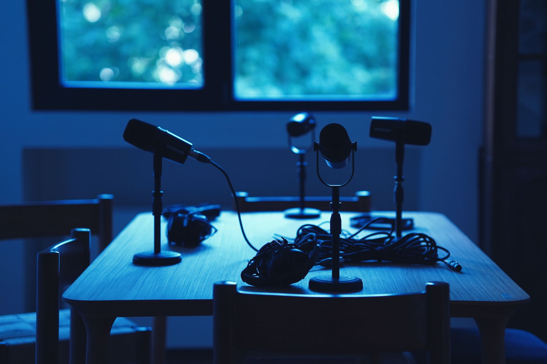 Four microphones and headphones sit on a wooden table in blue lighting