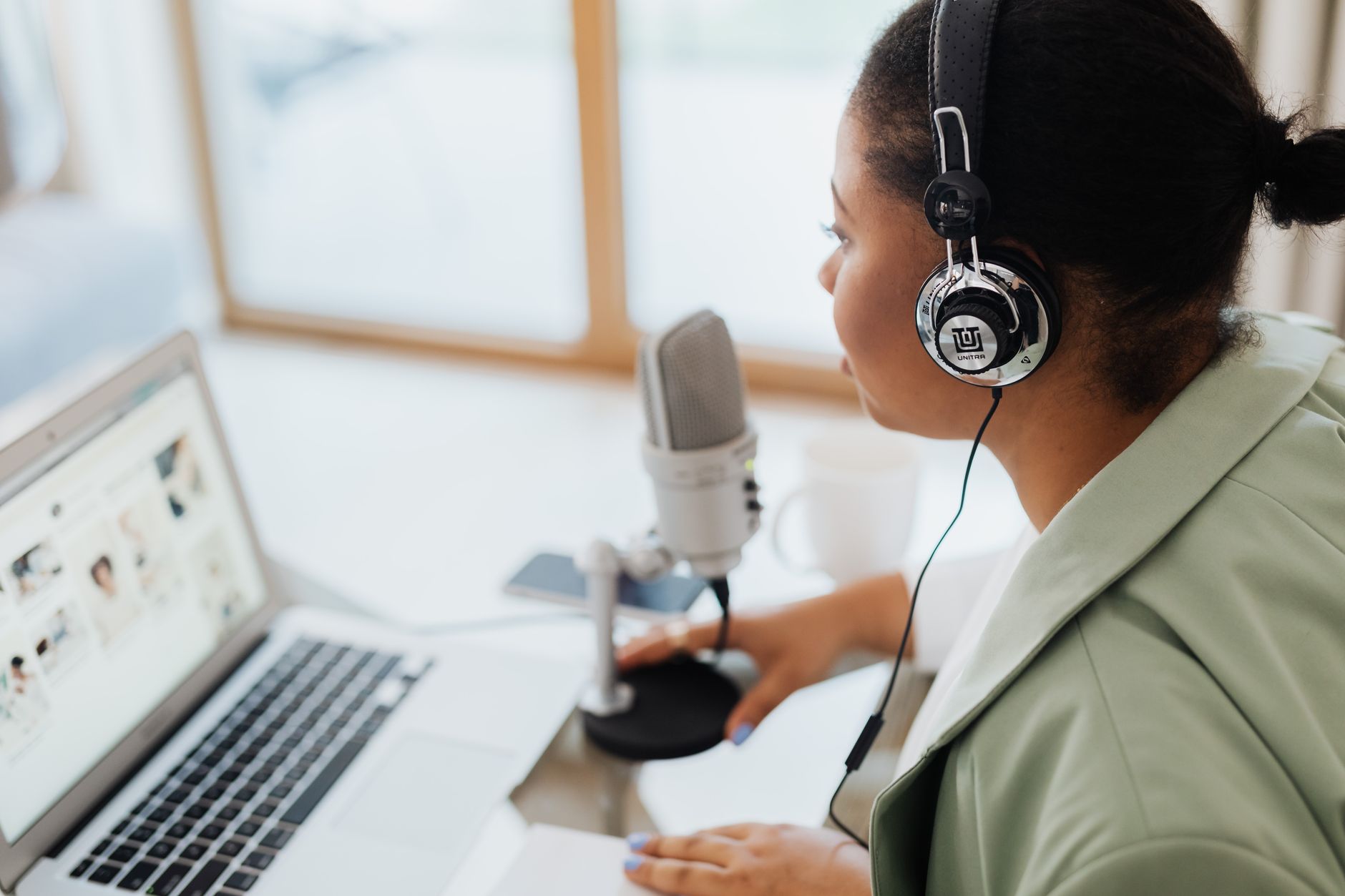 Person with headphones and microphone viewing a laptop for podcast analytics