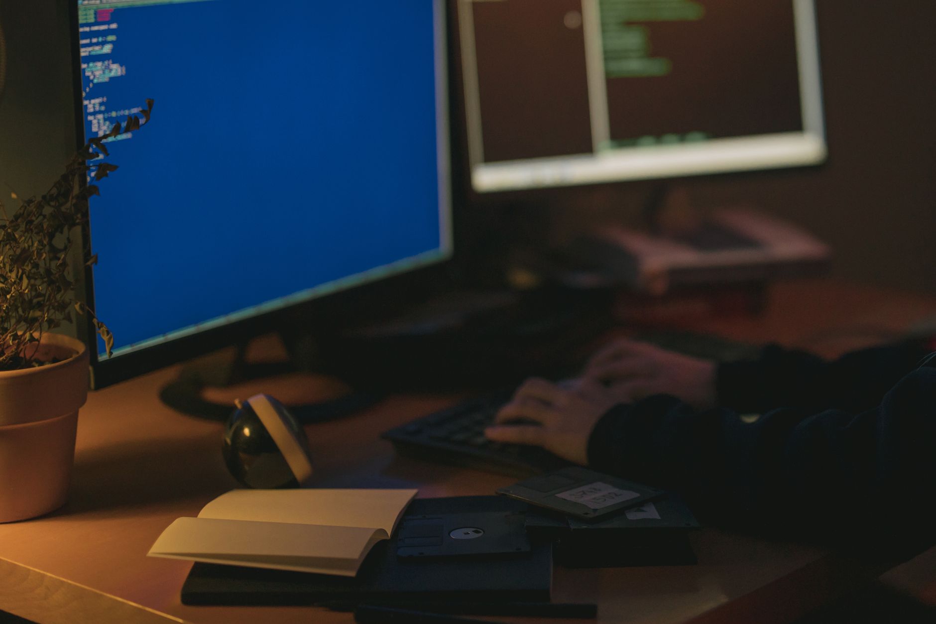 Hands type on a keyboard in front of glowing monitors displaying code