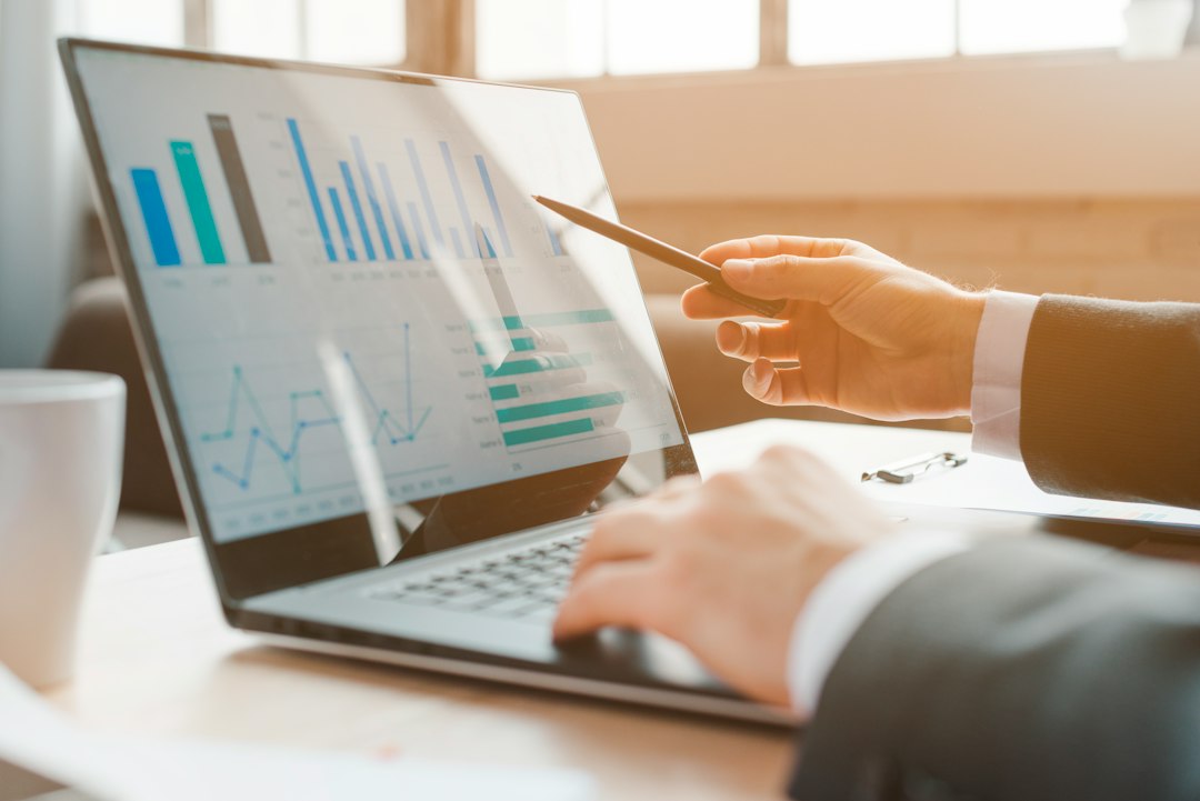 A person points a pen at charts on an open laptop screen