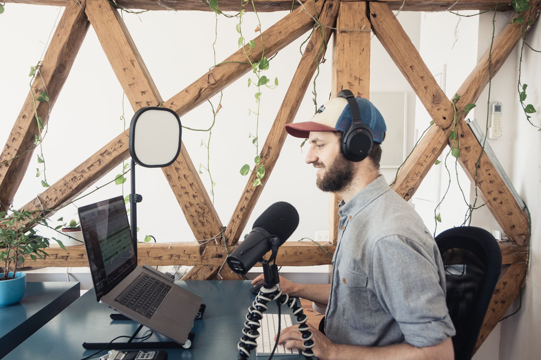 Man wearing headphones editing audio on a laptop with a microphone nearby
