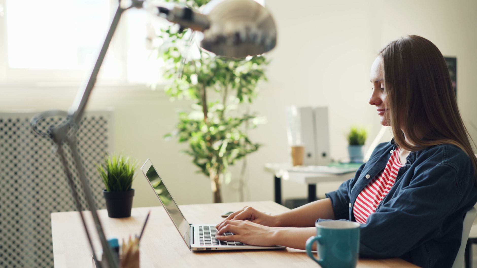 A woman types on a laptop at a wooden desk in an office