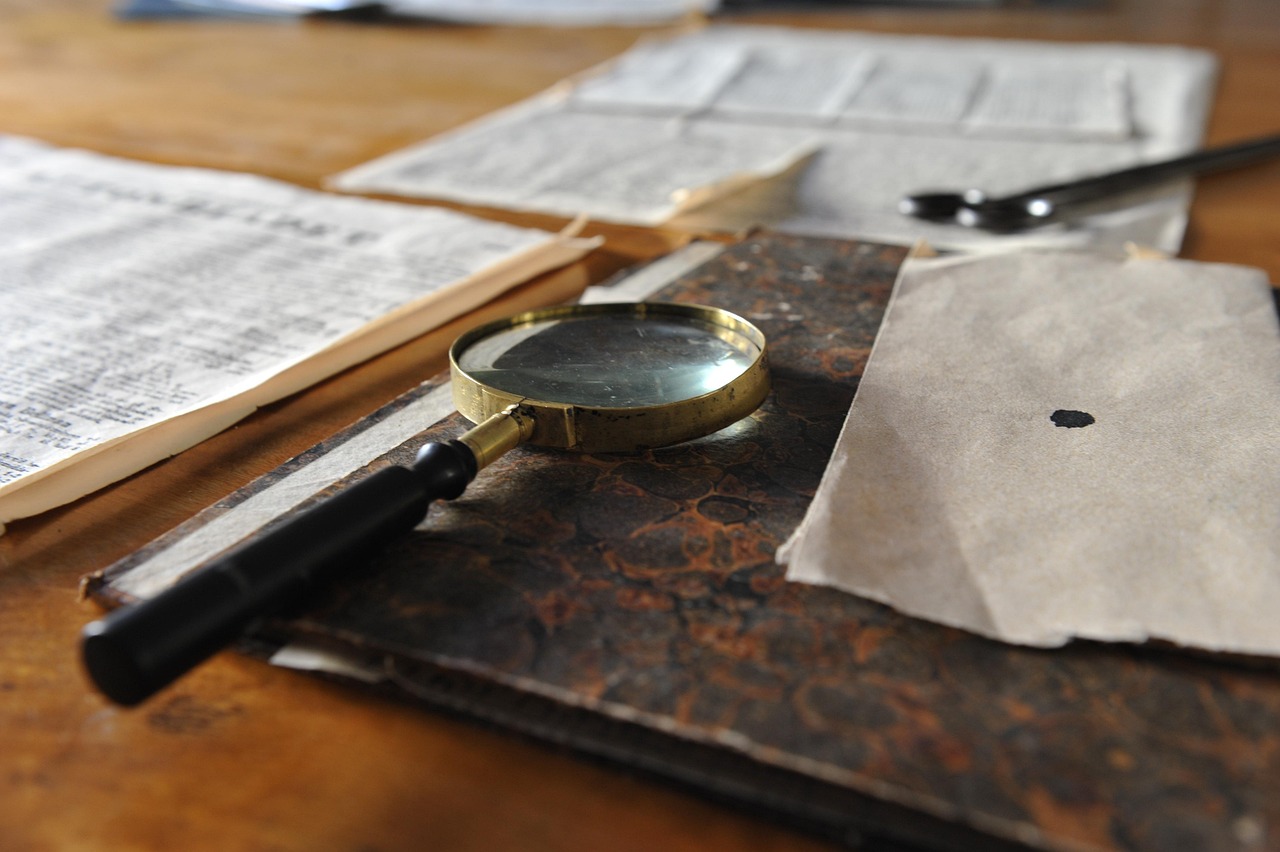A brass magnifying glass rests on an antique book and papers on a wooden table