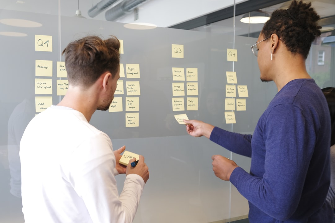 Two men strategizing with sticky notes on a glass board in an office