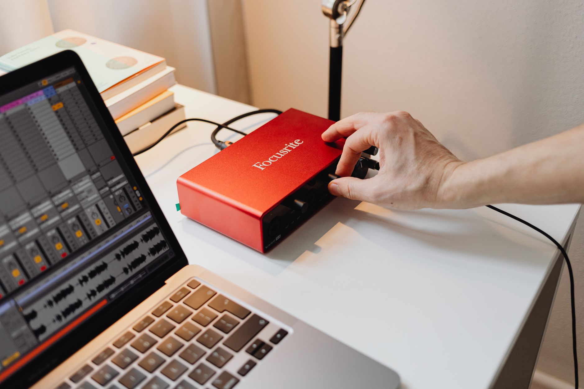 A hand turns a knob on a red audio interface beside a laptop