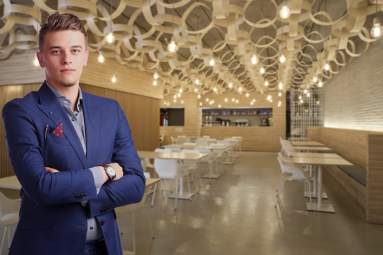 A confident man in a suit stands in a modern restaurant, representing business leadership