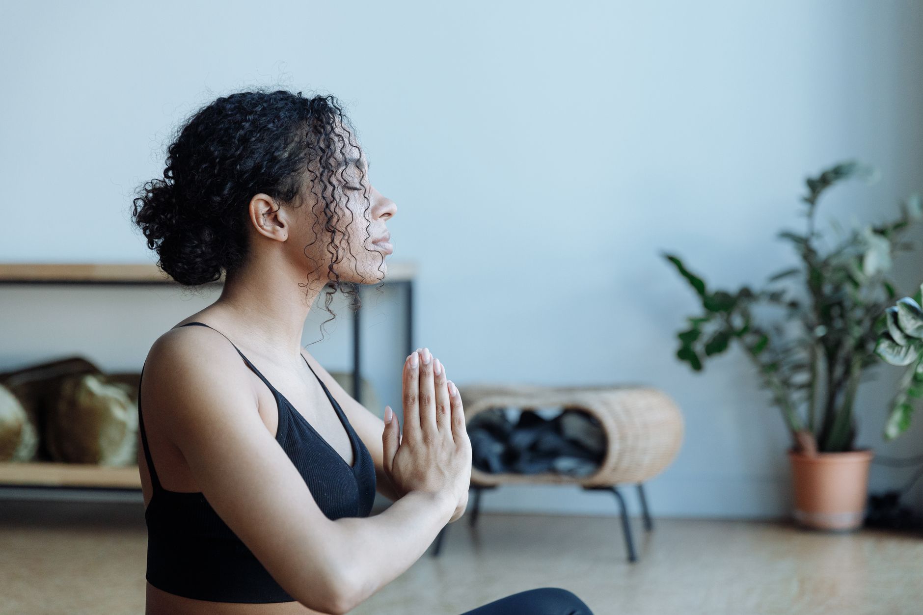 Young woman with curly hair meditating indoors with hands in prayer position