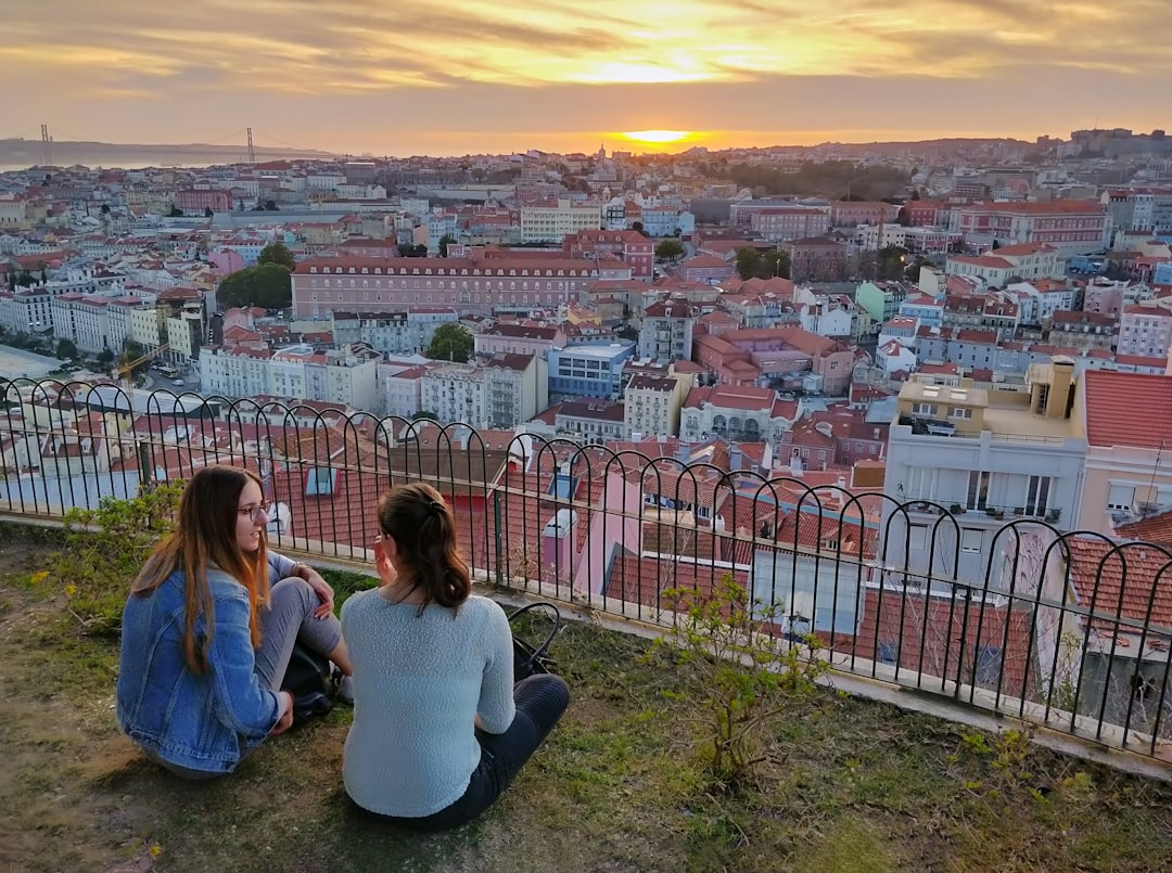 Two women enjoy a panoramic sunset view of Lisbon's cityscape from a hilltop