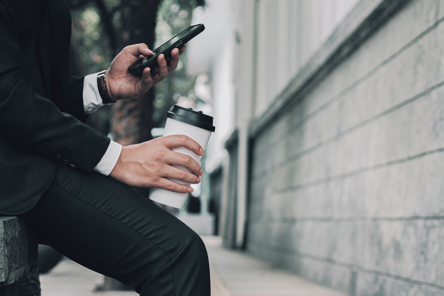 Person in a suit using a smartphone and holding a coffee cup outdoors