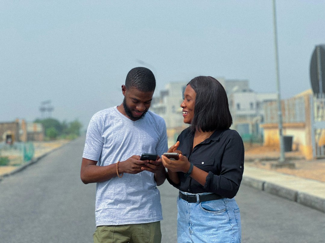 Two smiling people looking at smartphones, discussing something outdoors