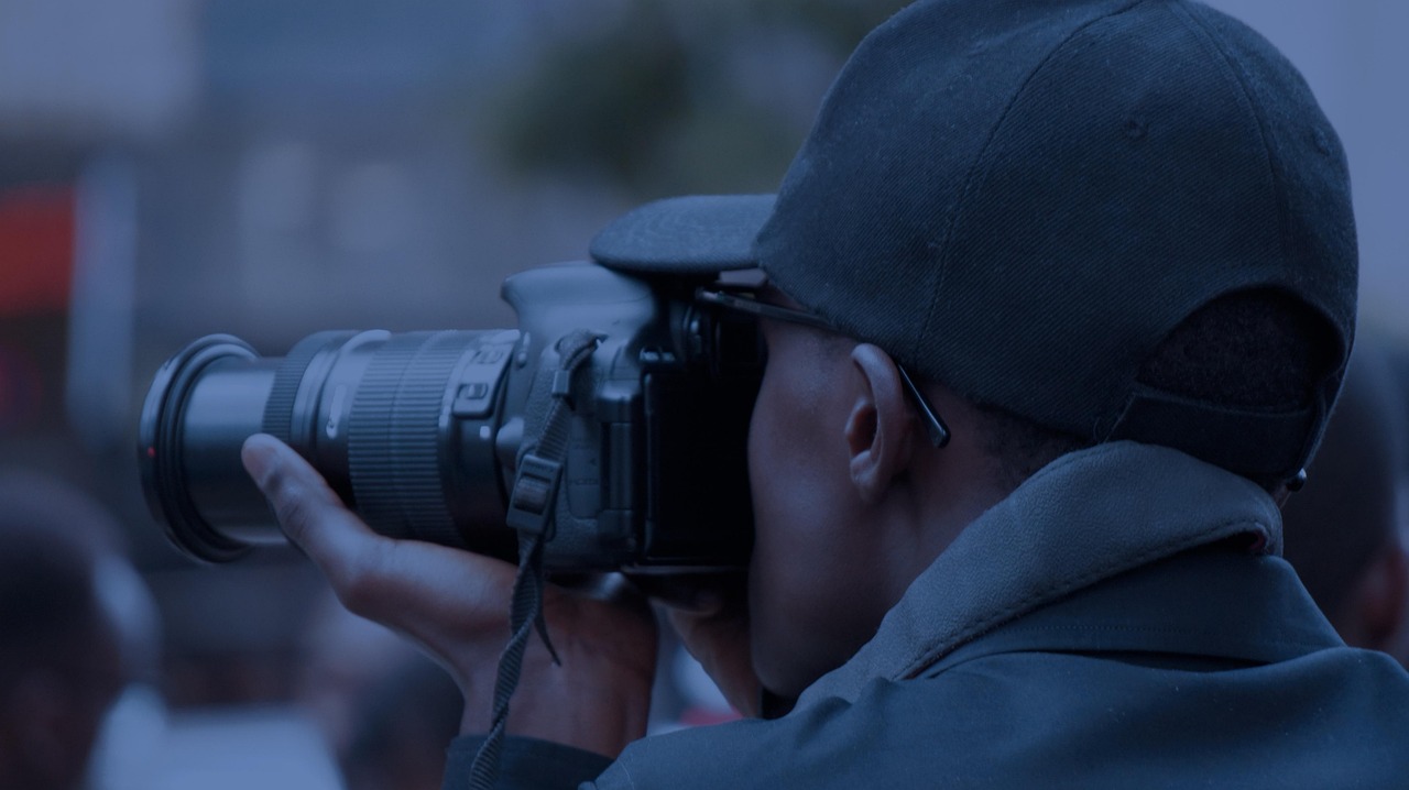 Person in a cap taking a photo with a large camera, looking through the viewfinder