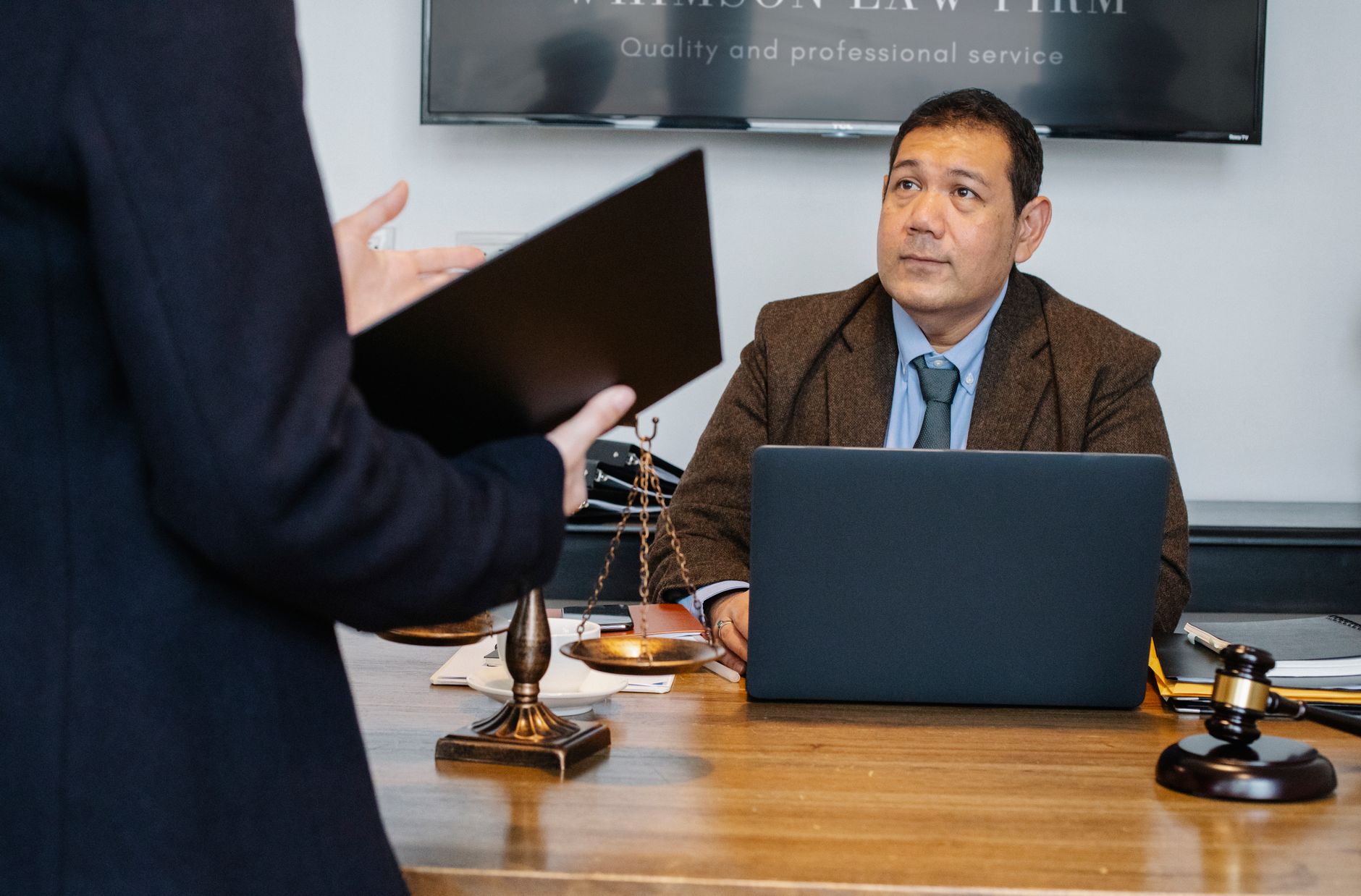A man in a brown jacket consults another person about legal fees in an office