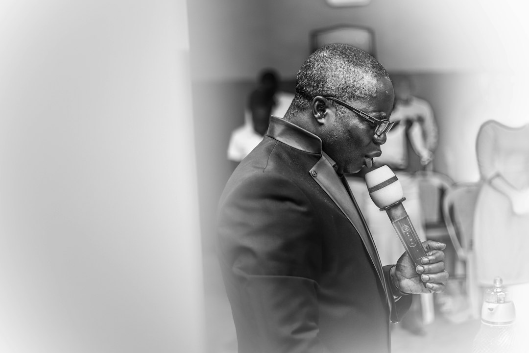 Black and white image of a man in glasses speaking into a microphone