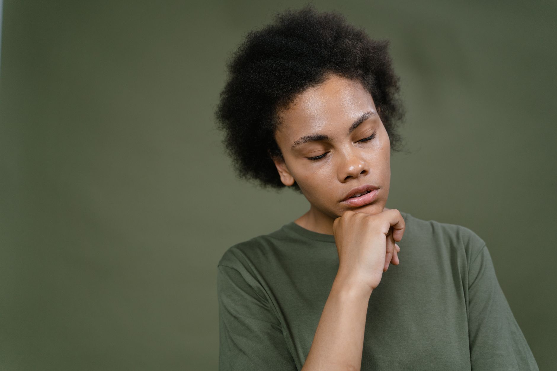 Young Black woman with eyes closed, hand on chin, contemplating trauma healing