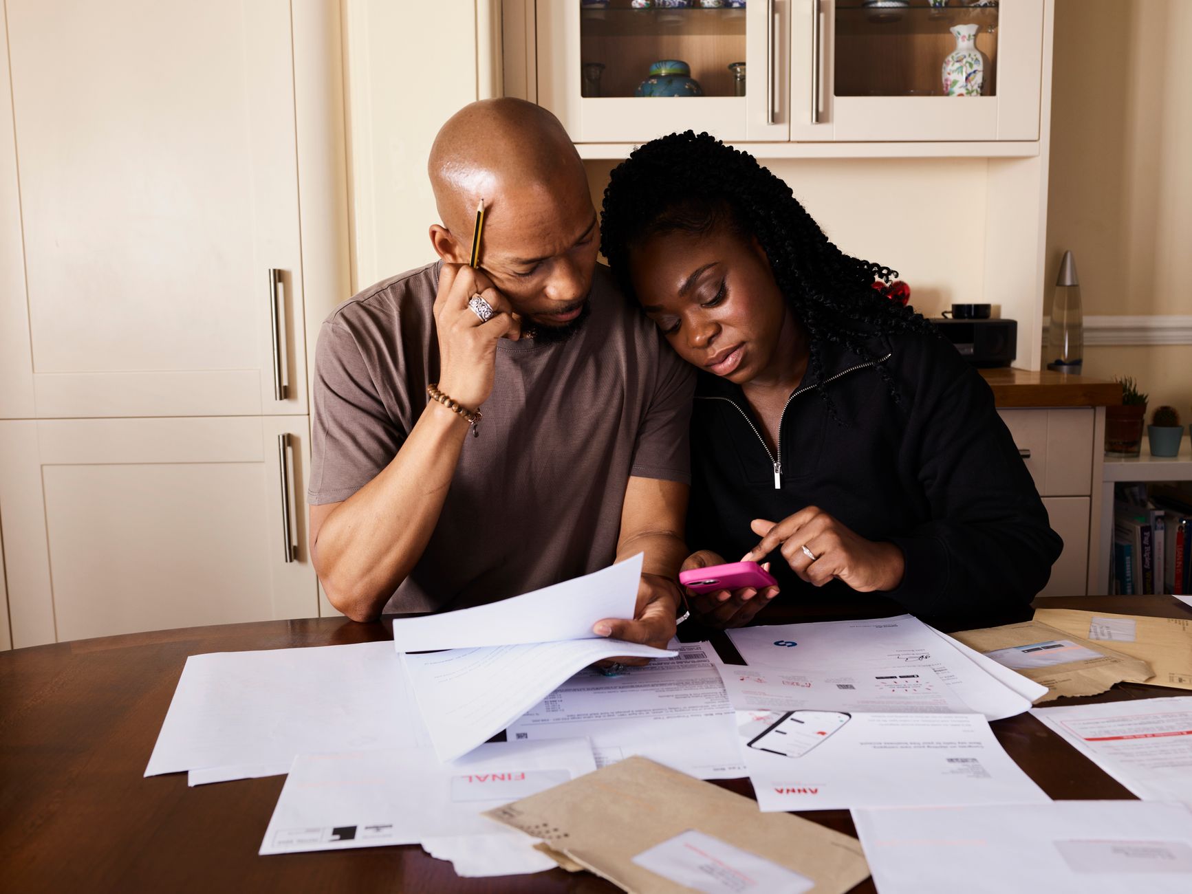 A couple budgets together, reviewing documents and using a smartphone at a table