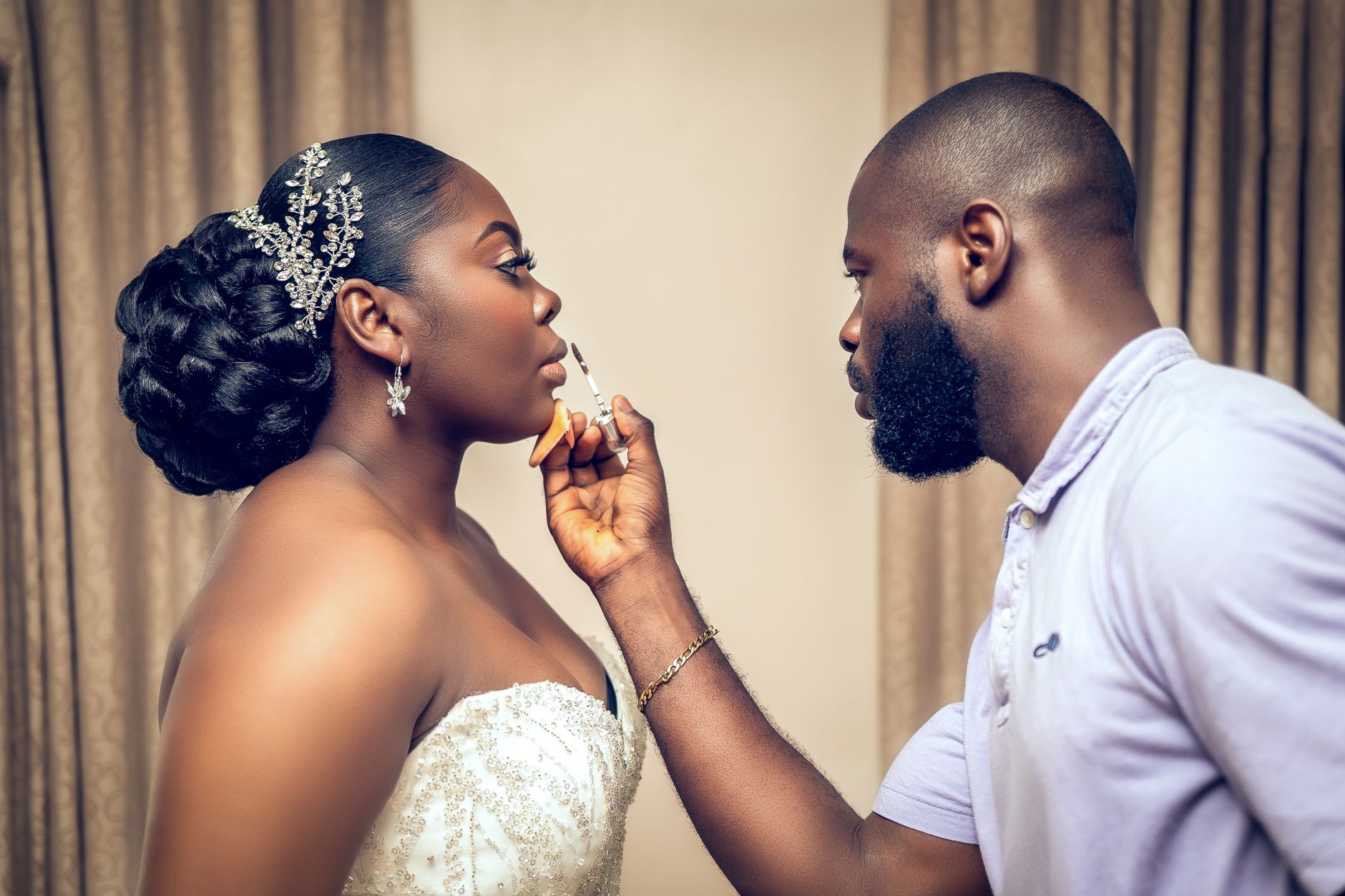 A makeup artist applies lipstick to a bride in a white wedding gown