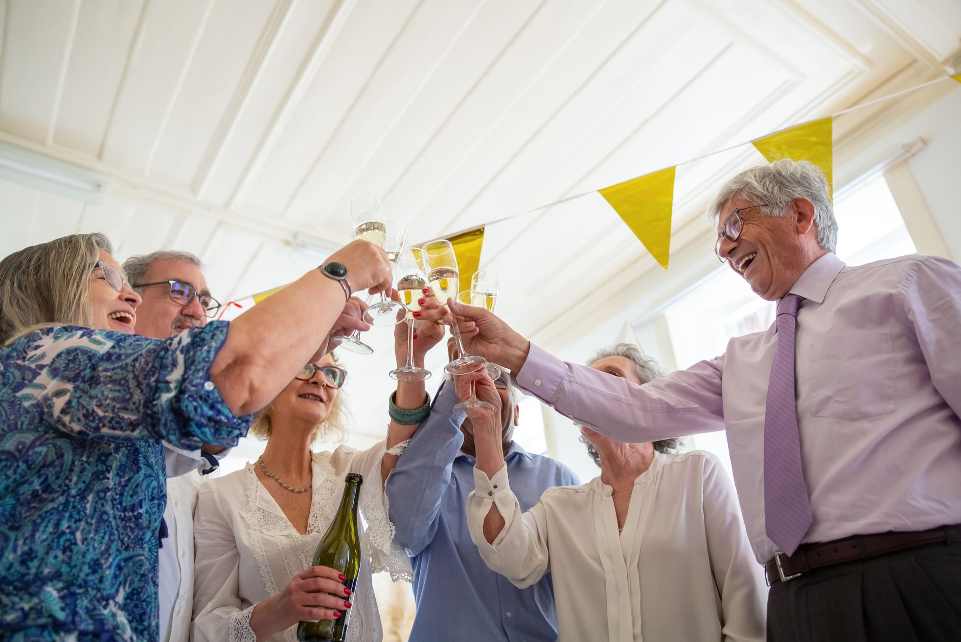 Smiling older friends raise champagne glasses, celebrating together under party bunting