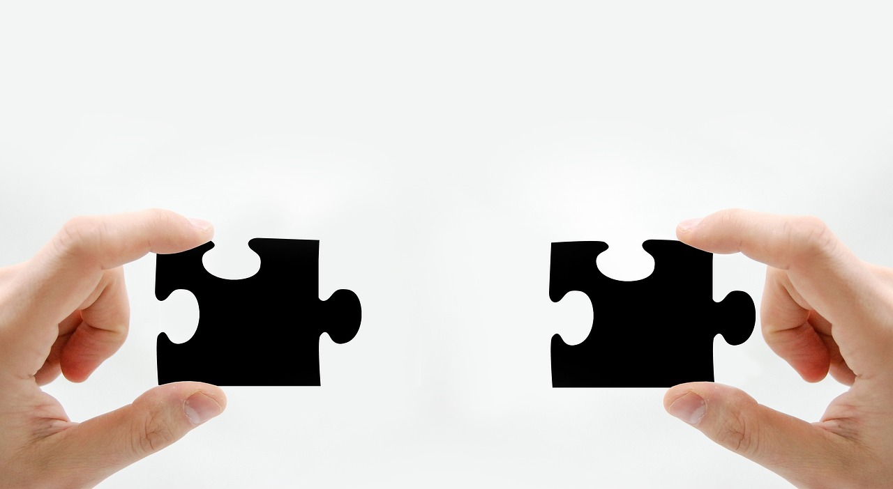 Two hands hold black puzzle pieces, illustrating connecting SEO efforts and business outcomes