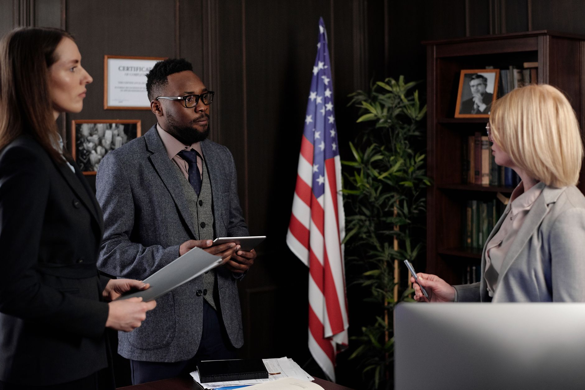 Three legal professionals discussing documents and tablets in an office setting