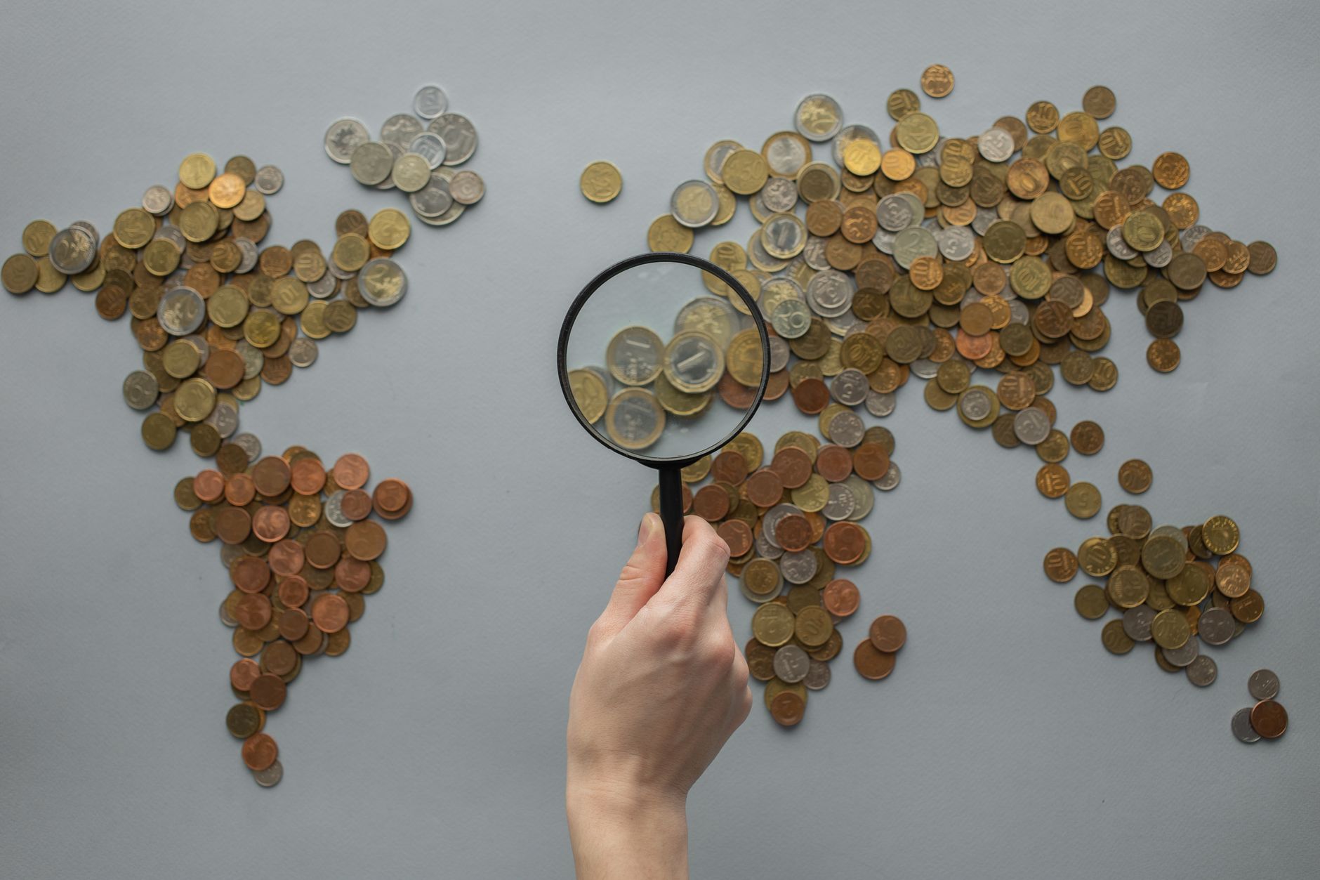 Hand holding a magnifying glass over a map of the world made of coins